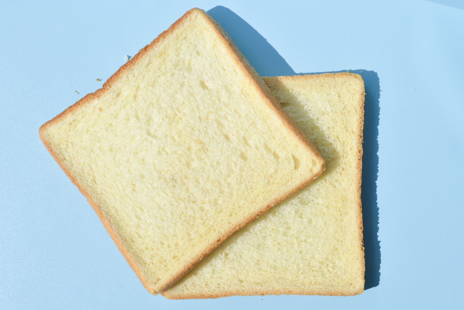 Two slices of white sandwich bread on a light blue surface.