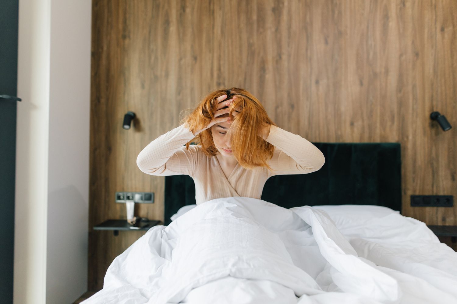 A person struggling to sleep in a bedroom, illustrating the link between insomnia and headaches.