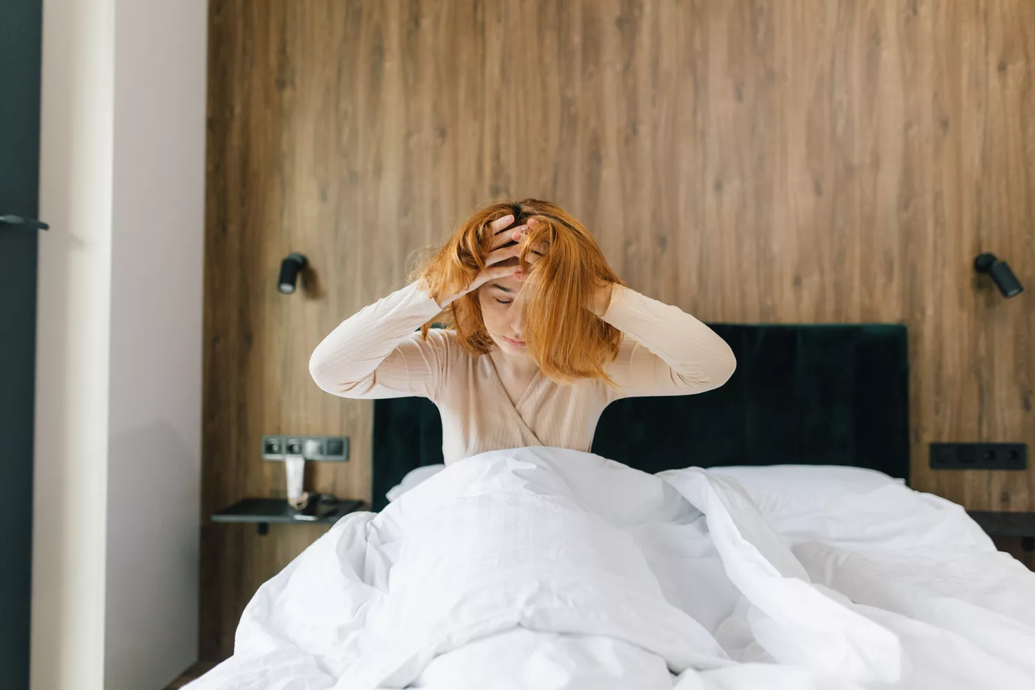 A person sitting in bed holding their head in discomfort during a migraine attack.