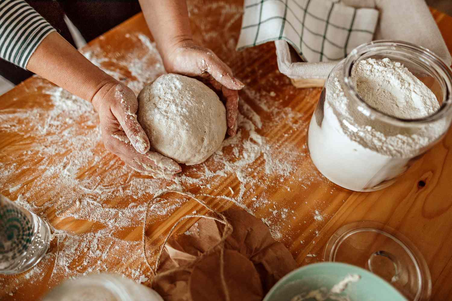 Hands kneading dough on a floured wooden table, representing the artisanal baking process.