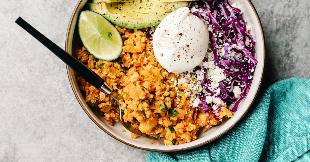 A vibrant keto bowl featuring cauliflower rice, avocado, lime, poached egg, and purple cabbage.